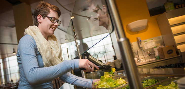 Woman putting lettuce on plate at Washakie Dining Center salad bar