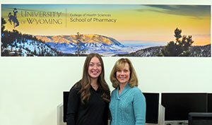two women standing under a School of Pharmacy banner