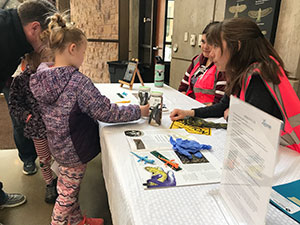 children looking at educational materials on a table run by people in orange vests