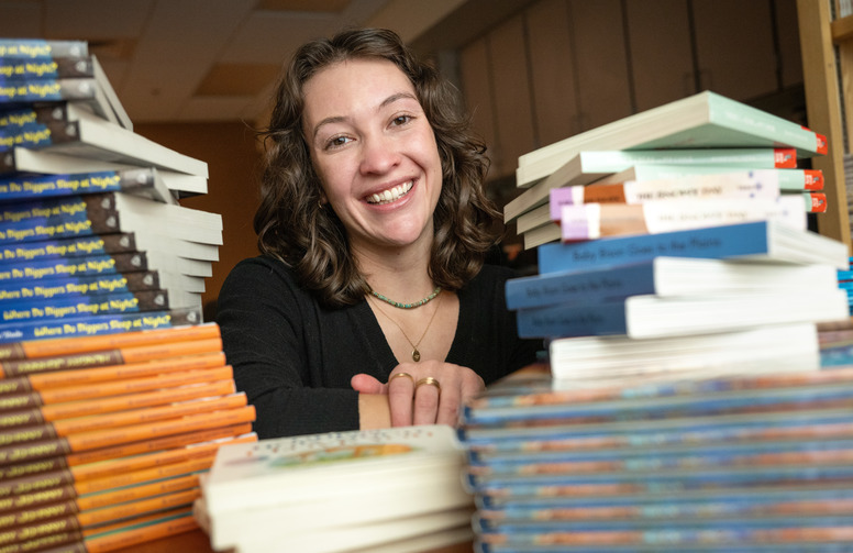 student with large stacks of books smiling.
