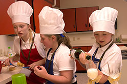 Three young girls wearing white chef hats and cooking.