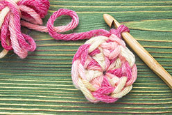 Pink and white yarn with crocket needle on green background