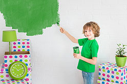 Girl painting white wall with green paint.
