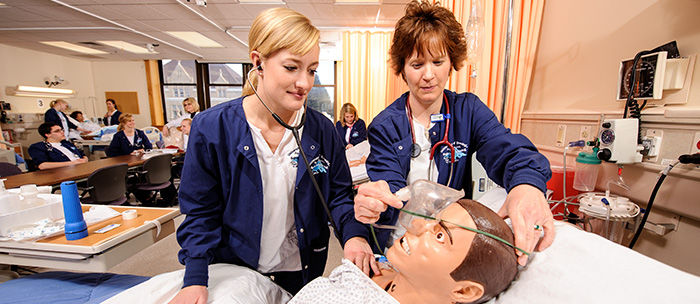 two women nursing students check lung sounds and apply face mask to manikin in skills lab