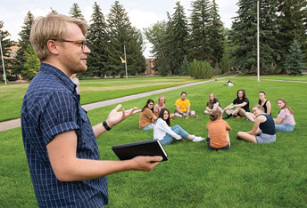 man speaking to people sitting in circles on the grass