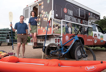two people with outdoor recreation equipment by a camper