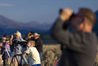people using binoculars by a mountain lake