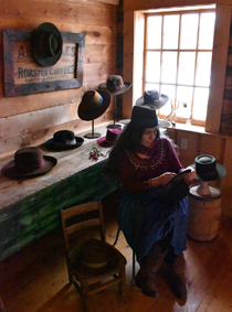 woman making a hat in a room displaying other hats