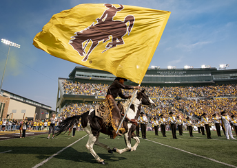 person riding a horse and holding a large UW flag on a football field