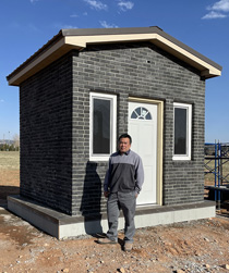 small gray brick house with a man standing in front of it