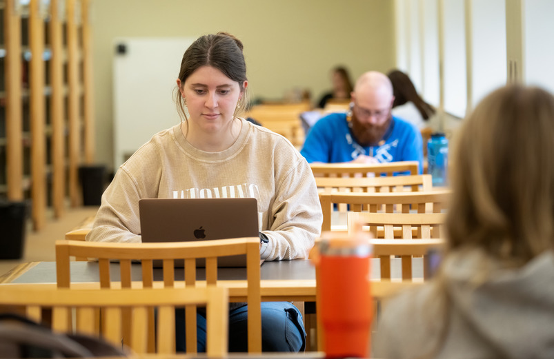 A student studies at their computer while sitting a table.
