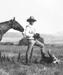 Man standing with a foot preached on a cow skull and horse standing behind