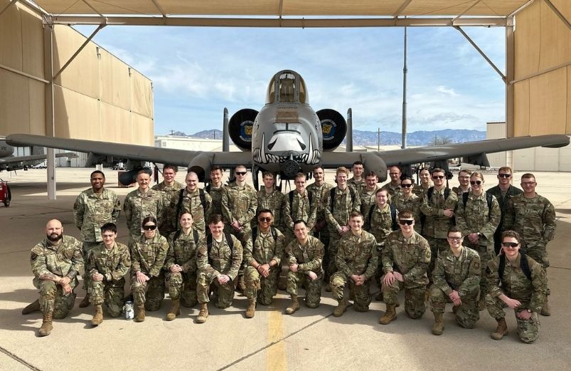 Air Force ROTC members pose in front of a military jet inside an airplane hanger.