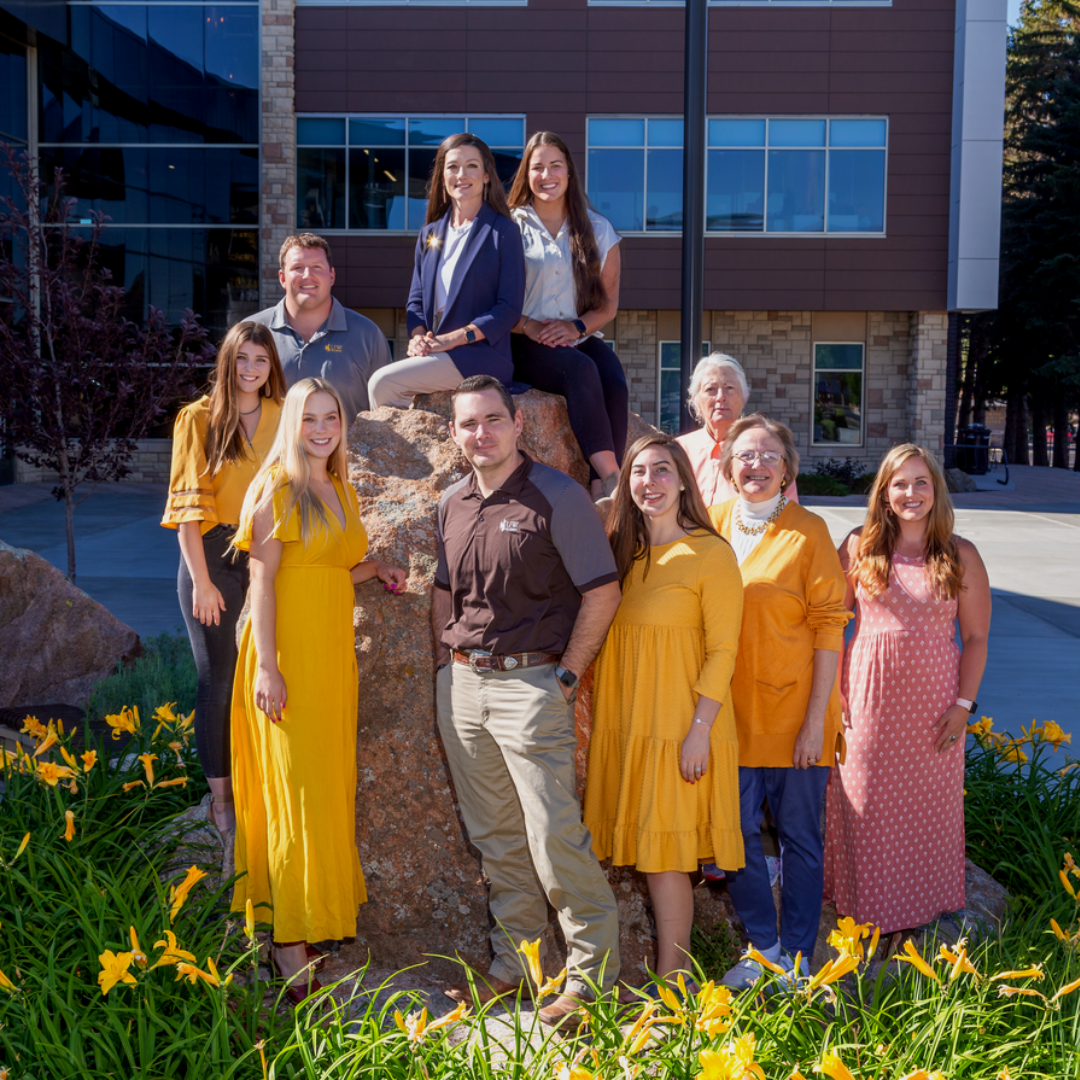 UWAA Staff sitting staggered on rock in front of Marian Rochelle Gateway Center