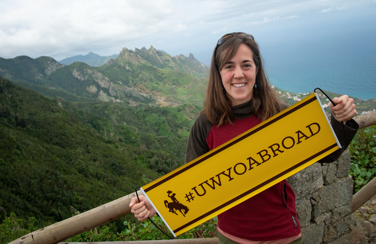 Student holding a study abroad banner at a scenic outlook point.