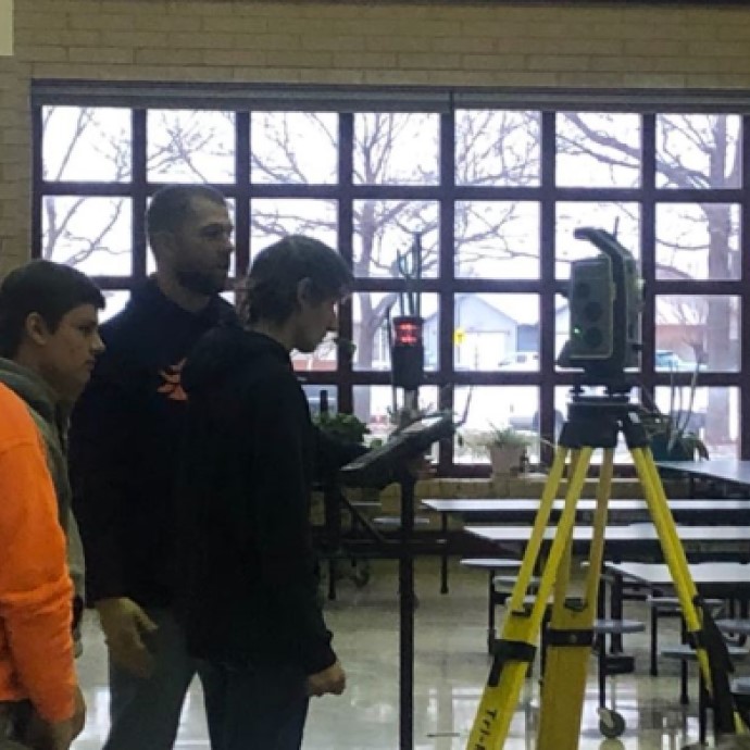 A professional land surveyor teaching a group of young students.