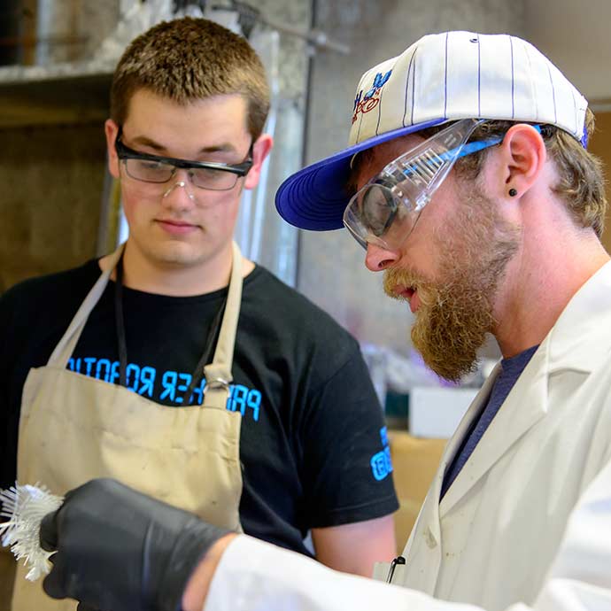Man and student in safety goggles examine materials in engineering lab