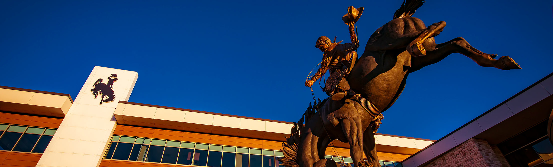 Bronze statue of cowboy on a bucking horse, in front of the Gateway building