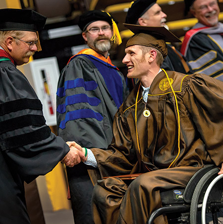 A student in a wheelchair accepts his diploma in a graduation ceremony.