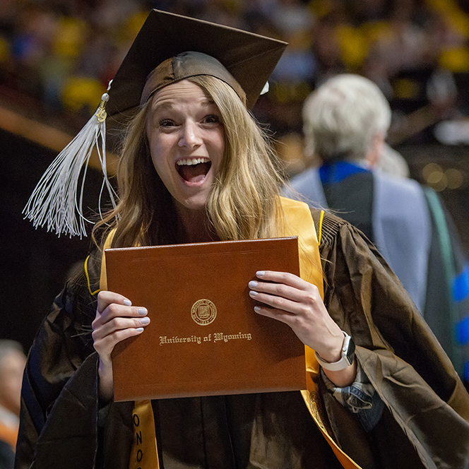 A student celebrates during commencement while holding their diploma