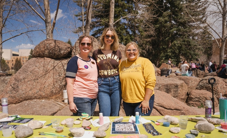 Three event organizers smile for a picture in front of their promotional table