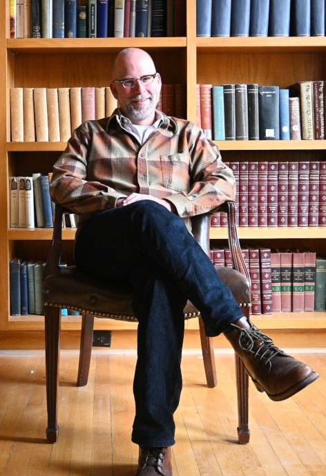 Man sits in a chair in front of bookshelves.