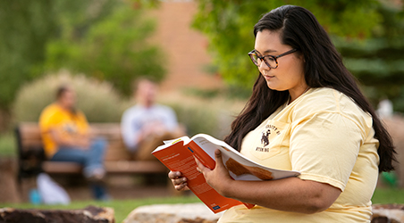 Student sits outside reading a book