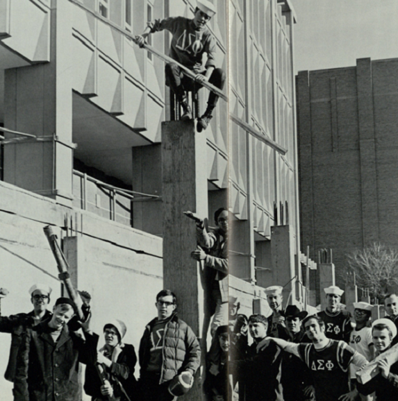 group of men standing outside the biological science building during it's construction. One man is standing on a pillar above the rest