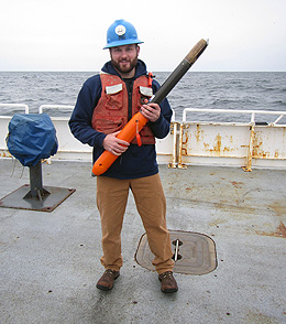 UW doctoral student standing on a ships deck holds an instrument called a uCTD.