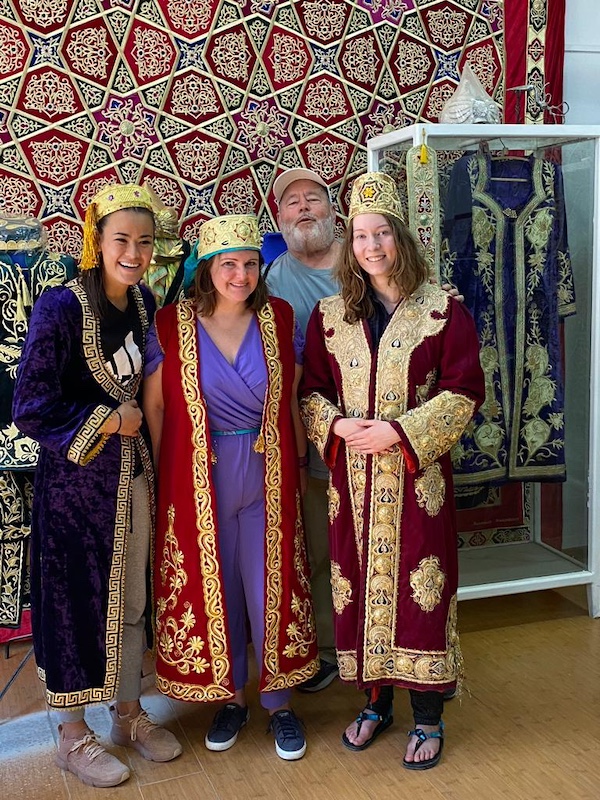 three women wearing Bukhara embroidery with a smiling man