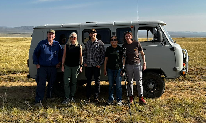 John, Isa, Nick, and Mongolia partners in front of a van in a prairie