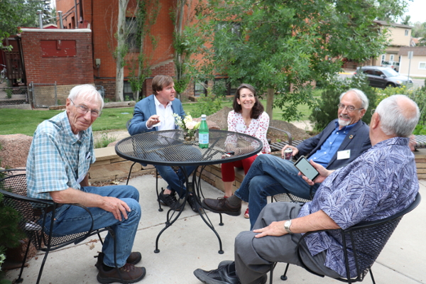 A group of attendees at Ruckelshaus Day tree dedication event sit around a table on the patio of the Bergman Gardens behind the Bim Kendall House.