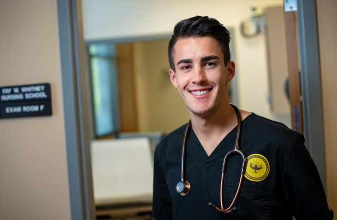 A Doctorate of Nursing Practice student in scrubs standing in front of an exam room 