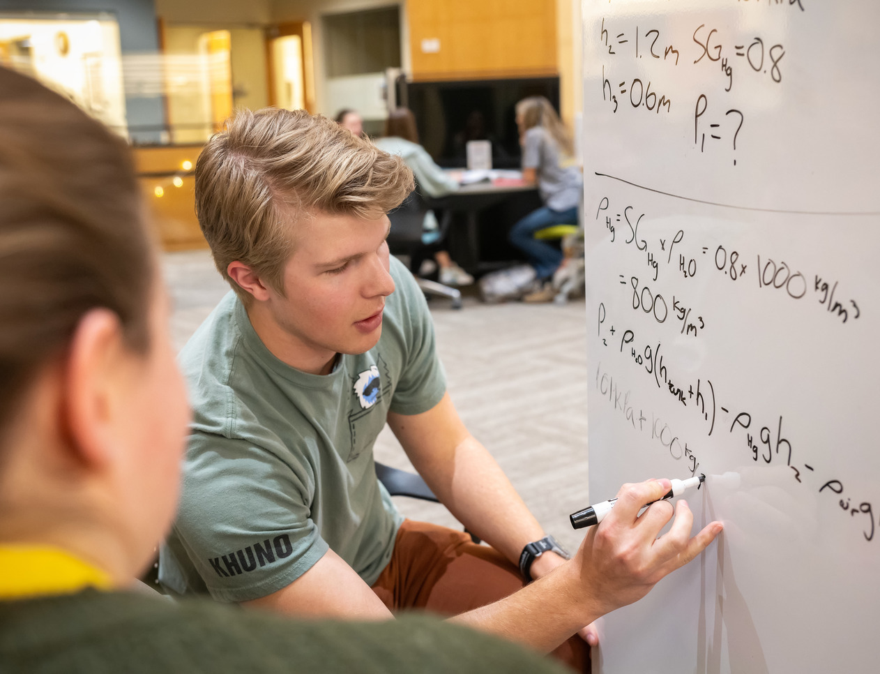 student in University of Wyoming Student Learning Commons STEP Tutoring writes math work on a whiteboard to help another student.