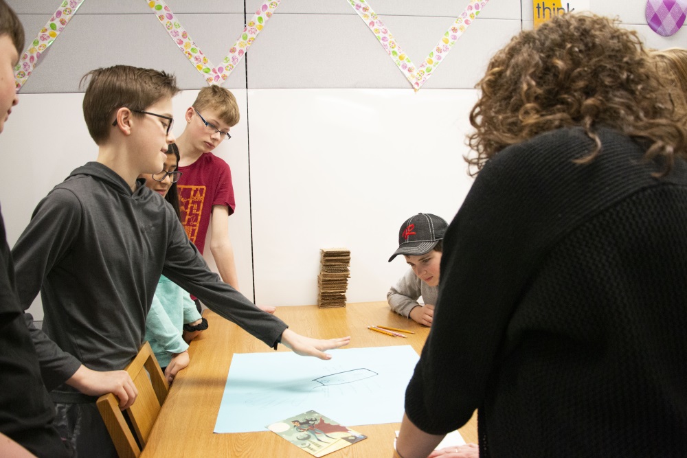 students and teacher standing at table discussing book creation project