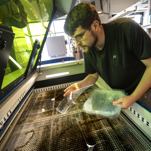 a student uses a laser cutter in the UW machine shop to cut acrylic components for research
