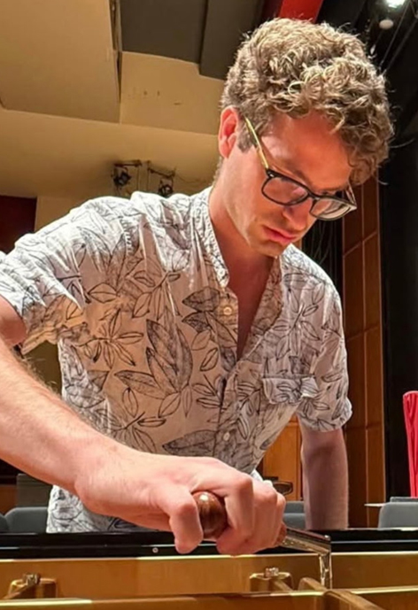 Serious young man in glasses tuning a piano.