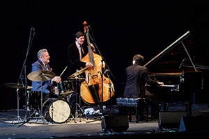 musicians with drum set, string bass and piano performing on stage
