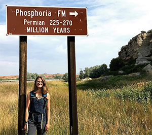 woman standing under a sign pointing to a rock formation