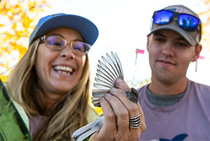 woman holding a bird with wing extended while a man looks on