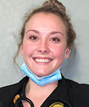 smiling face of young woman in clinical garb with facemast around her neck
