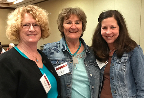 three women smiling at camera wearing their convention badges and wide smiles