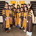 12 elated graduate students dressed in brown and gold academic regalia