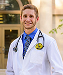 Noah standing outside the Health Sciences Center in white lab coat and stethoscope