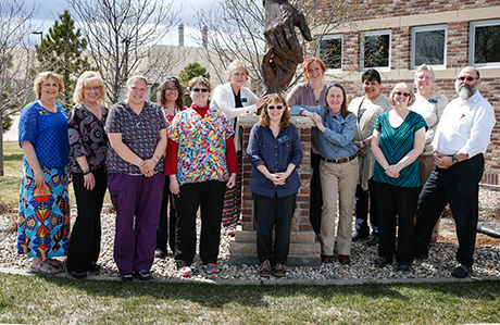 12 women and one man stand with a statue in front of the LCCC building