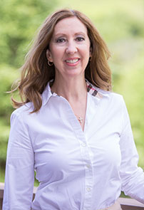 woman with long flowing brown hair, white blouse, with green leafy background