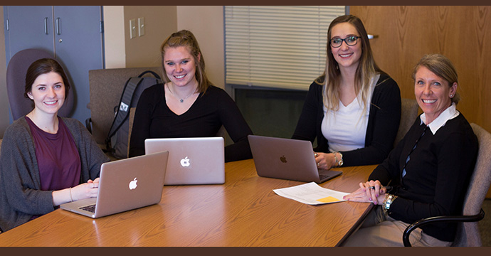 three female students and Dr. Thomas sit at table with laptops