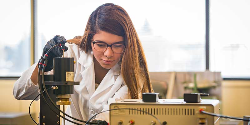 Woman in lab coat checks gauge in engineering lab
