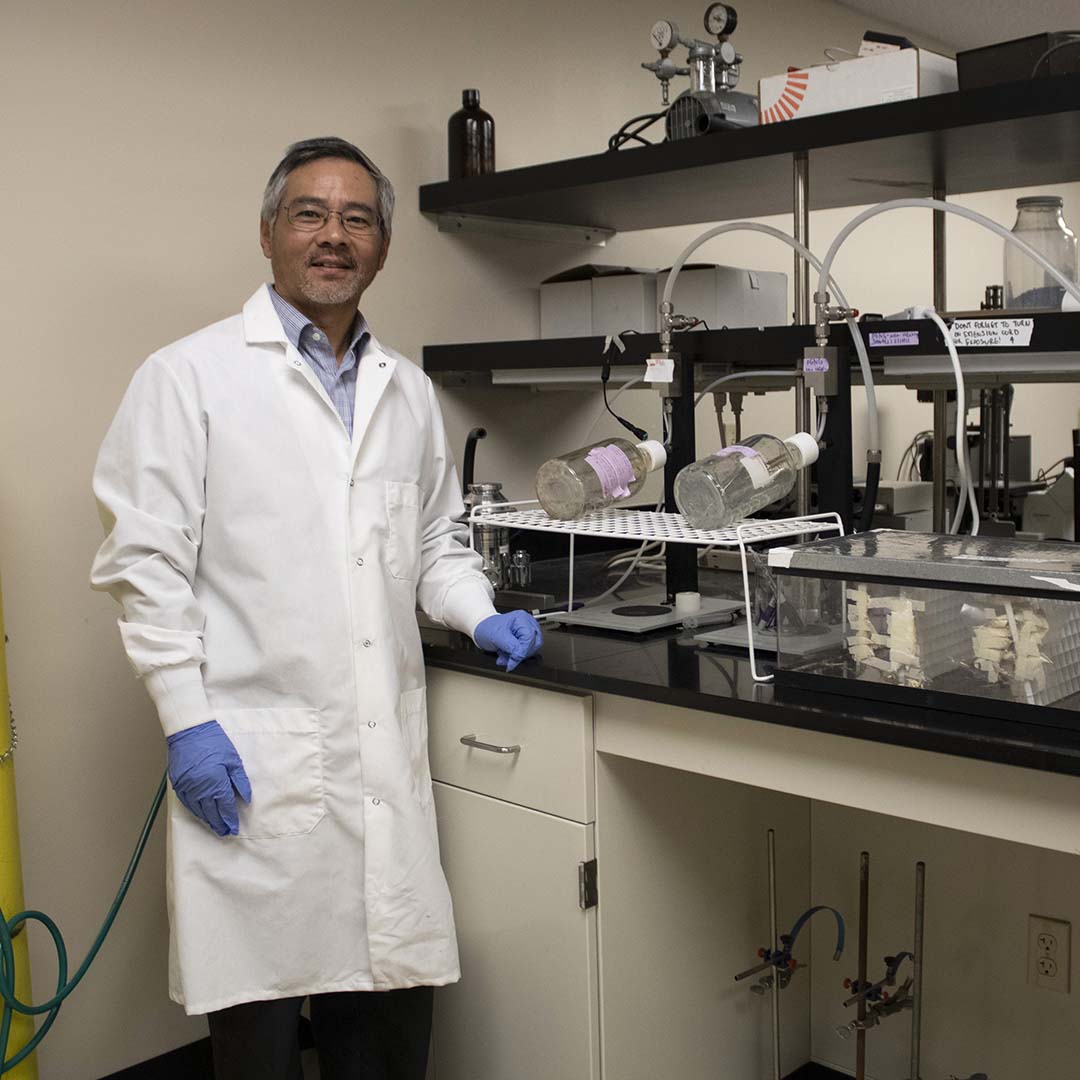 Man standing in a white lab coat inside a lab.