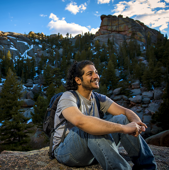 Male student sitting on a rock with turtle rock formation in the distance